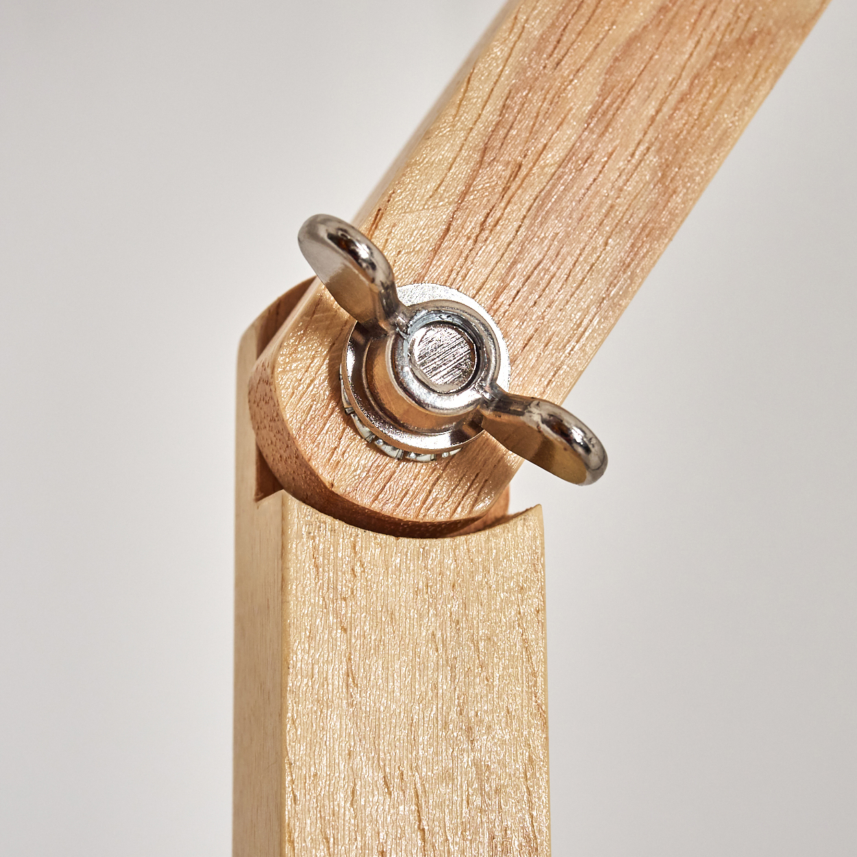 Nahaufnahme eines Holzgelenks mit einer Flügelmutter aus Metall. Das Holz ist hell und der Hintergrund ist weiß.