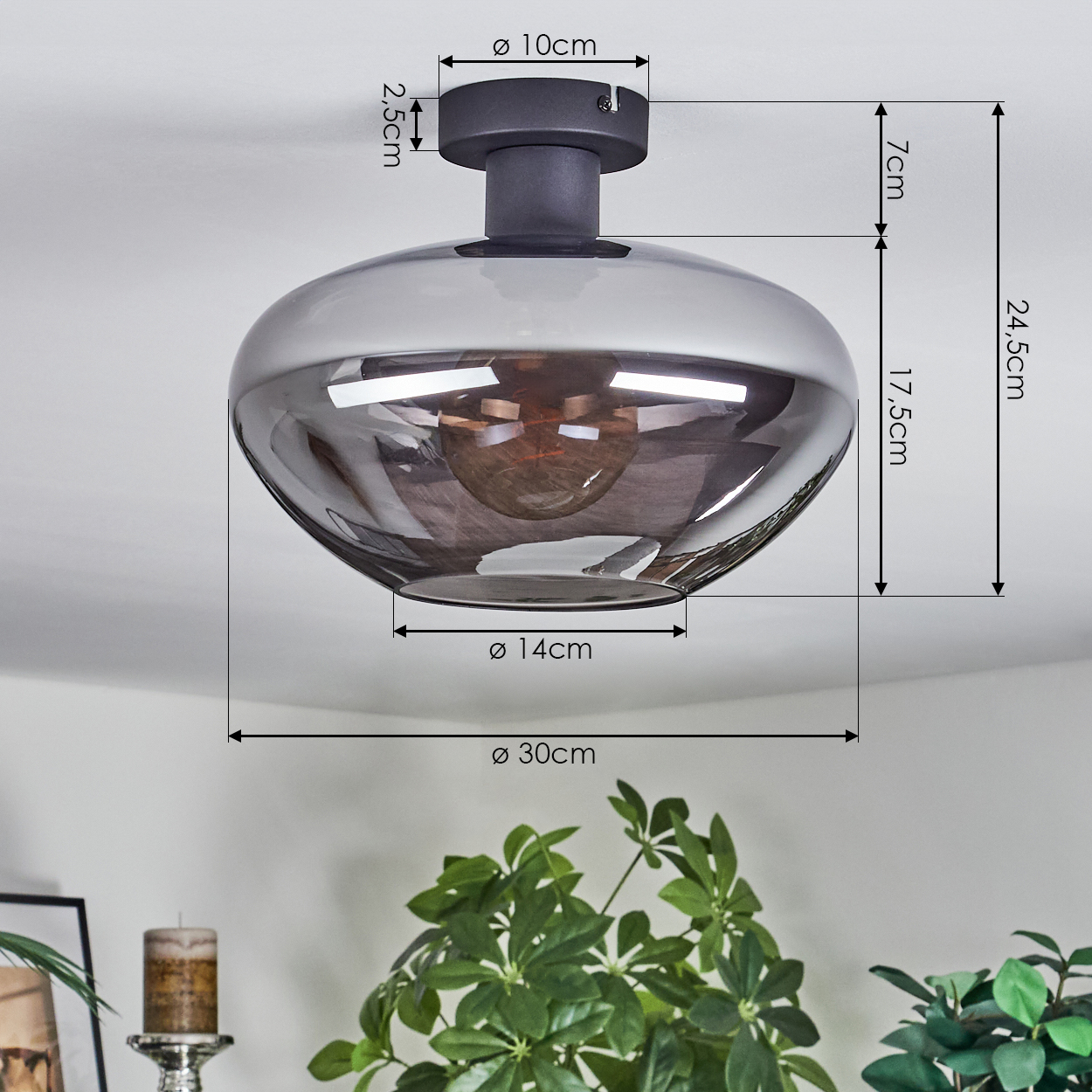 Graue Deckenlampe mit Maßangaben. Darunter grüne Pflanzen und eine Kerze sichtbar.