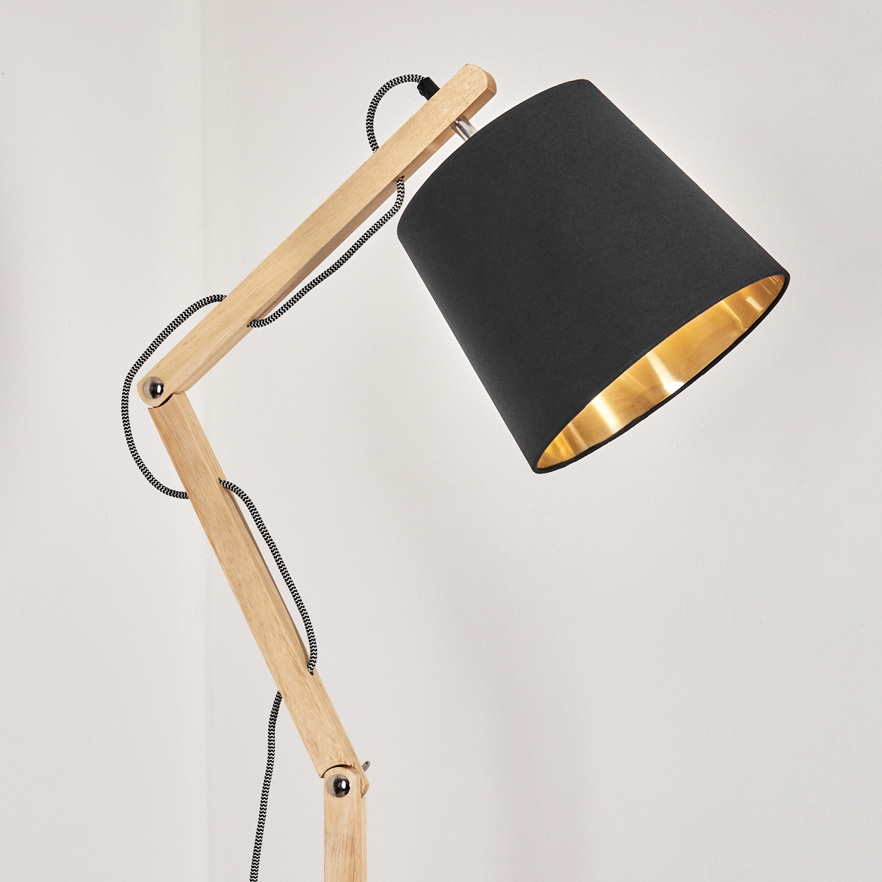 Eine Stehlampe aus Holz mit schwarzem Lampenschirm und goldenem Innenraum. Die Lampe hat einen flexiblen Arm und ein schwarz-weißes Kabel.