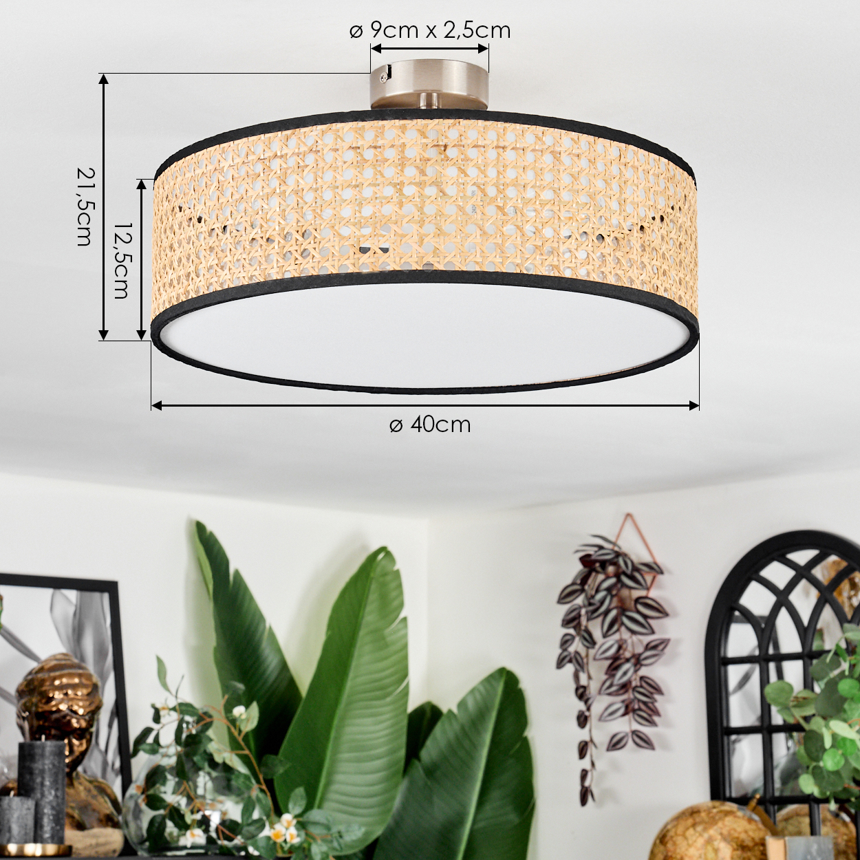 Eine runde Deckenlampe mit einem Schirm aus geflochtenem Rattan und schwarzem Rand. Im Hintergrund sind grüne Pflanzen und andere Dekorationen zu sehen.