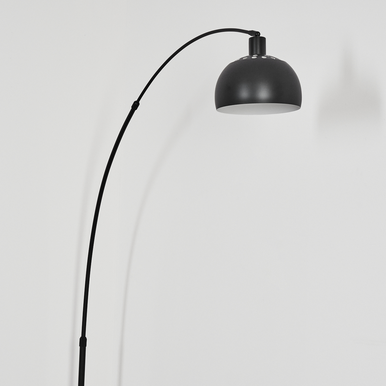 Eine schwarze Bogen-Stehlampe vor einer weißen Wand. Die Lampe hat einen kuppelförmigen Schirm und einen gebogenen Arm.