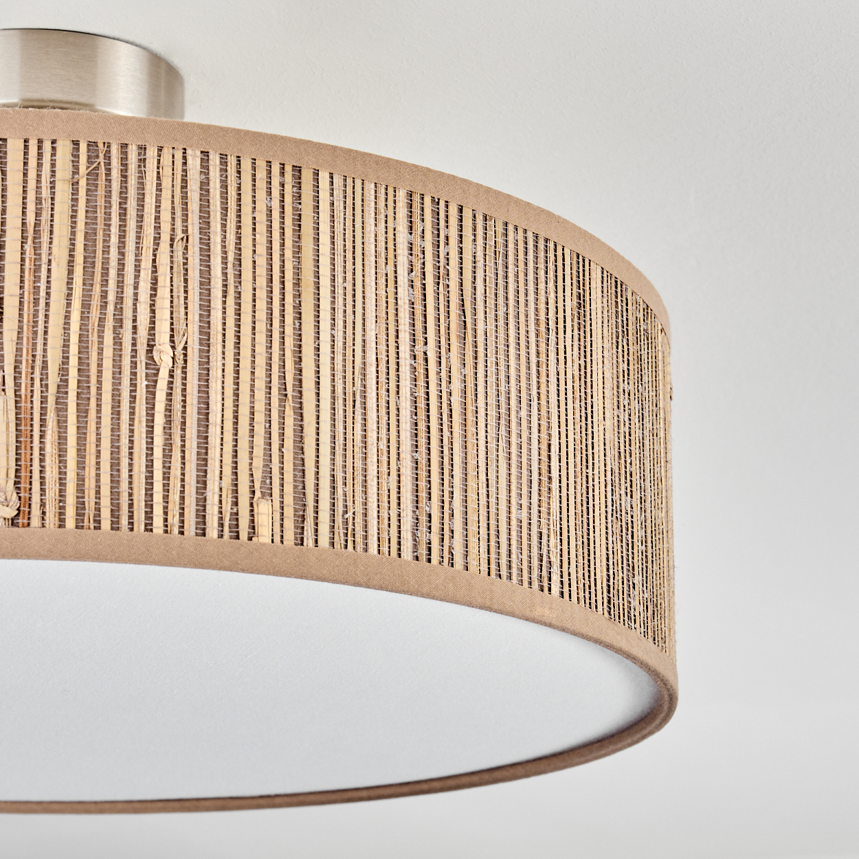 Nahaufnahme einer beige-braunen Lampe. Die Lampe hat einen gewebten Schirm mit weißem Boden und silbernem Oberteil, an weißer Decke montiert.