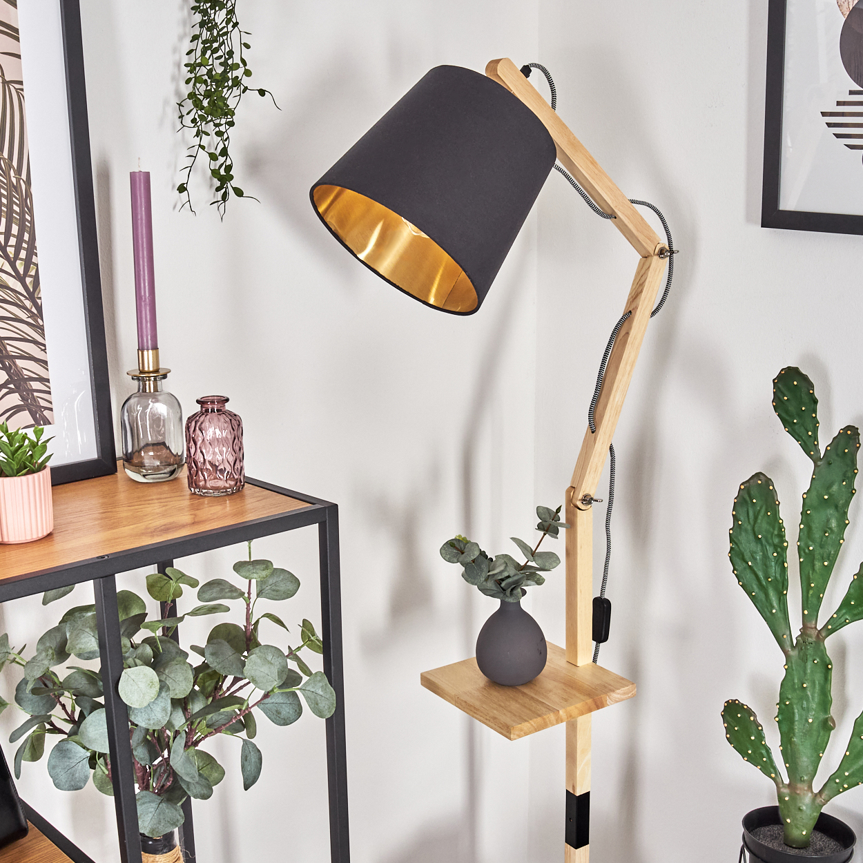 Eine moderne Holzlampe mit schwarzem Lampenschirm und goldfarbenem Innenraum. Ein kleiner Tisch hält eine Vase und eine Pflanze.