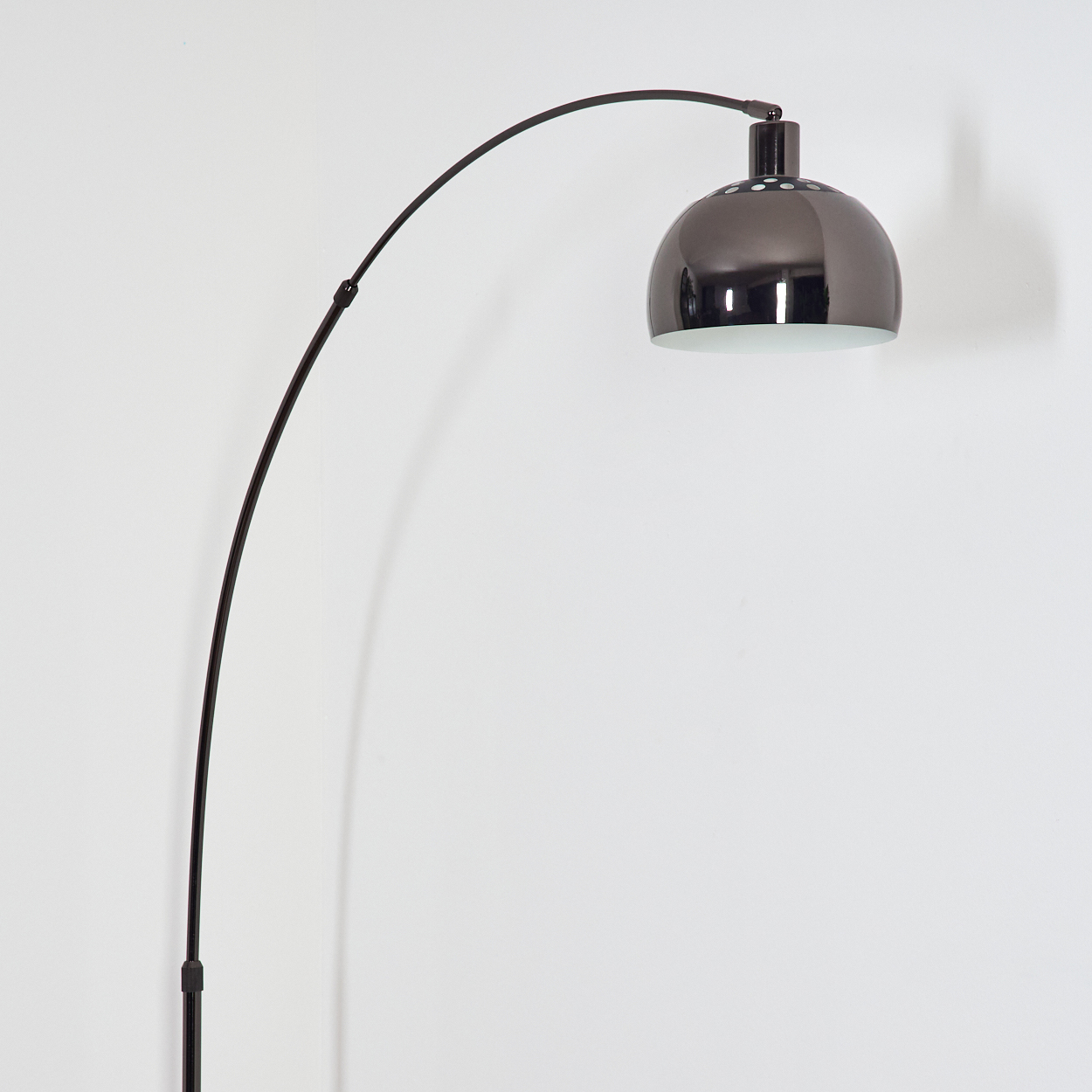 Eine moderne schwarze Bogen-Stehleuchte mit metallischem Schirm vor einer weißen Wand. Der Lampenstiel ist elegant gebogen.