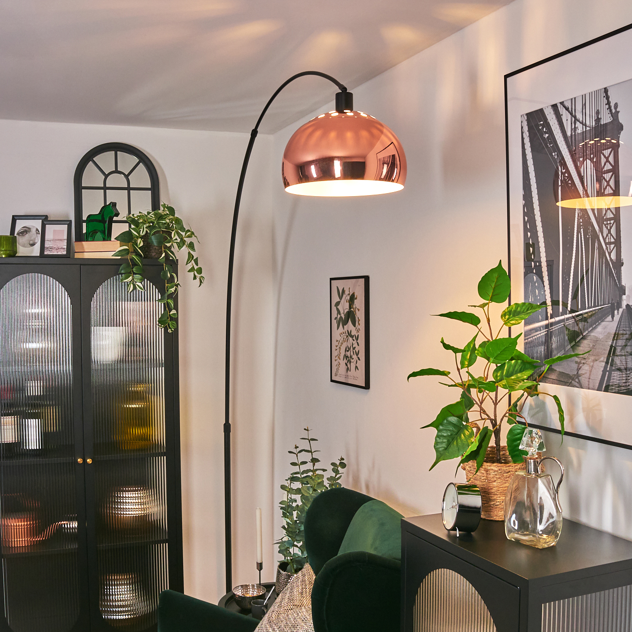 Ein modernes Wohnzimmer mit Kupferlampe, grünem Samtsessel und schwarzem Schrank mit verschiedenen Dekorationen.