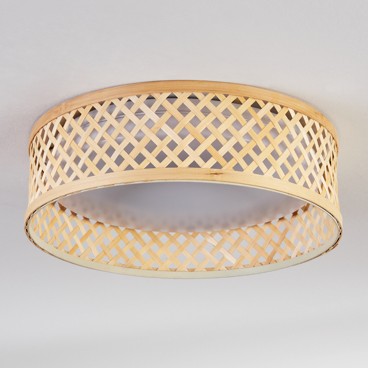 Eine runde Deckenlampe aus Bambus. Die Lampe hat ein gewebtes Design. Der Hintergrund ist eine weiße Decke.