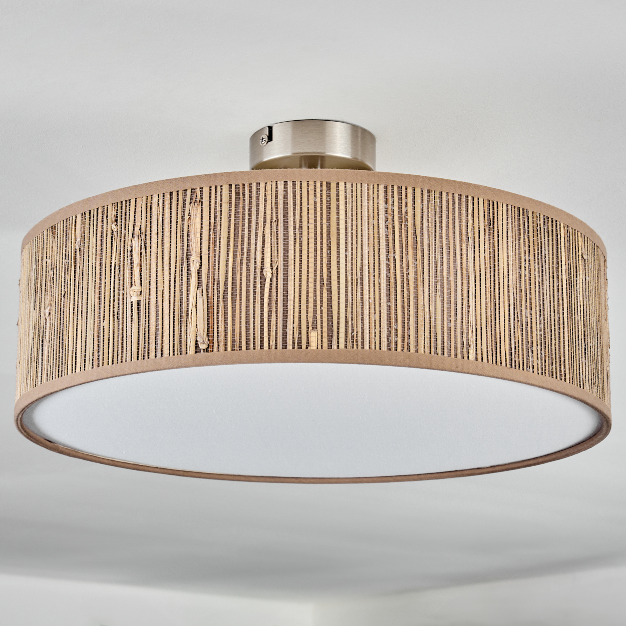 Eine runde Deckenlampe mit einem gewebten Bambusschirm und einem weißen Innendiffusor ist an einer weißen Decke montiert.