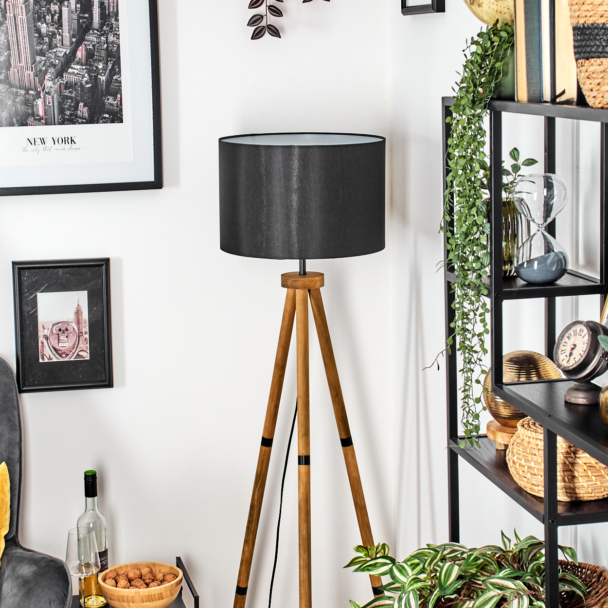 Ein Raum mit einer hölzernen Stativlampe mit schwarzem Lampenschirm, neben einem schwarzen Regal mit Dekorationen.