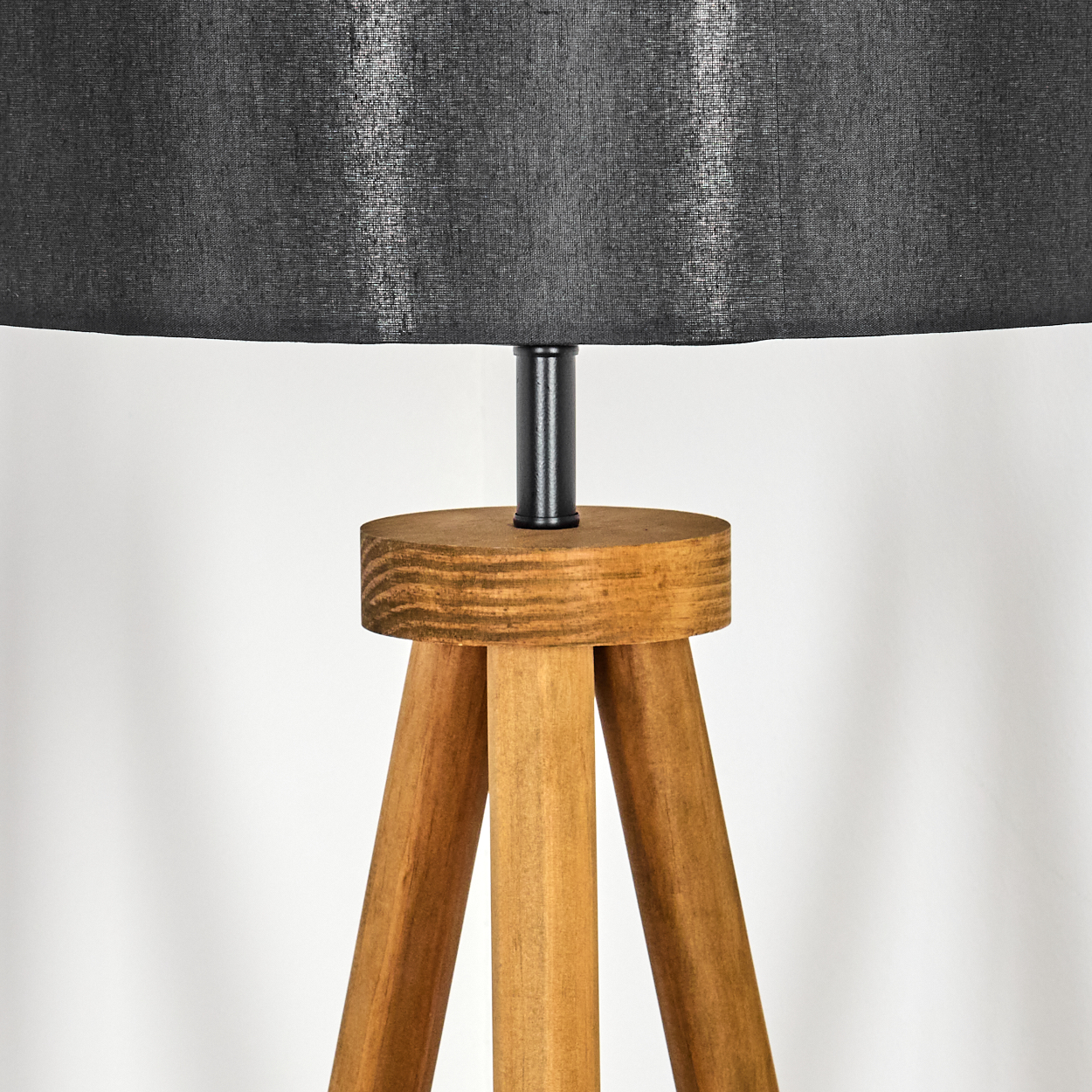 Nahaufnahme einer hölzernen Stativlampe mit schwarzem Lampenschirm. Die Lampe hat einen hellbraunen Holzfuß und eine schwarze Metallstütze.