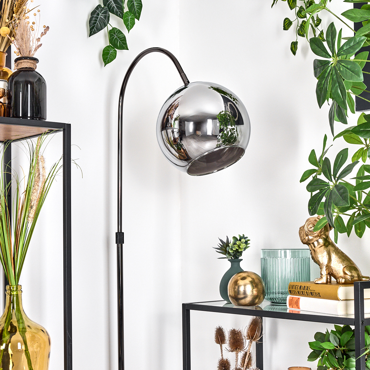 Moderne Chrom-Stehlampe mit kugelförmigem Kopf. Regale mit Vasen, goldener Bulldoggenstatue, Büchern und Pflanzen füllen die Szene.