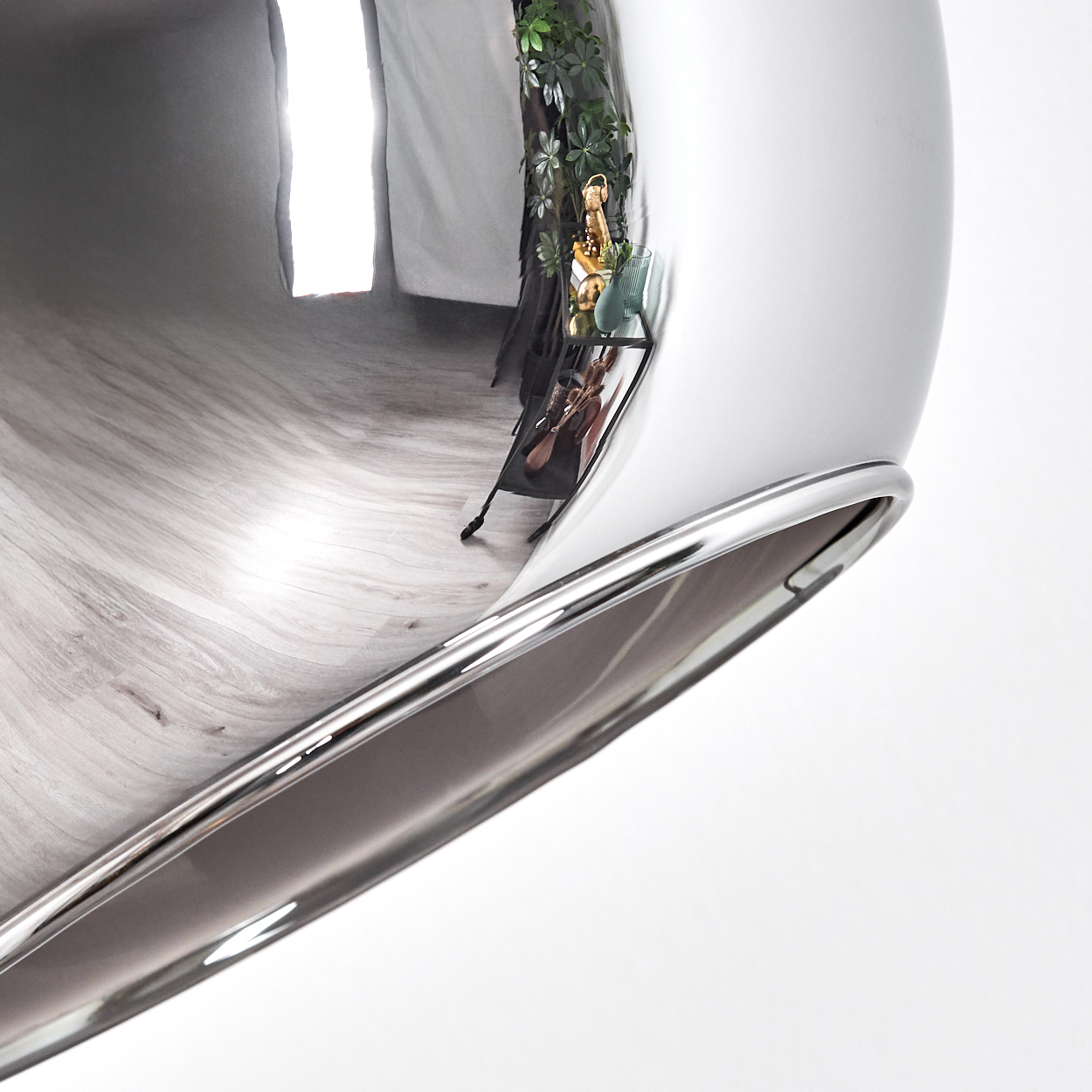 Ein glänzendes, gebogenes Chromobjekt reflektiert einen Raum mit Regal, Pflanzen und Holzboden. Ein weißer Hintergrund umgibt das Objekt.