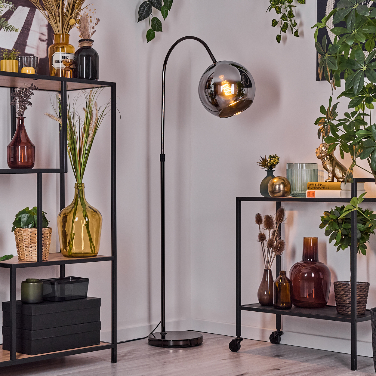 Ein Raum mit Regalen, Vasen, Pflanzen und einer schwarzen Stehlampe mit rundem Glasschirm. Der Raum hat ein modernes Design.