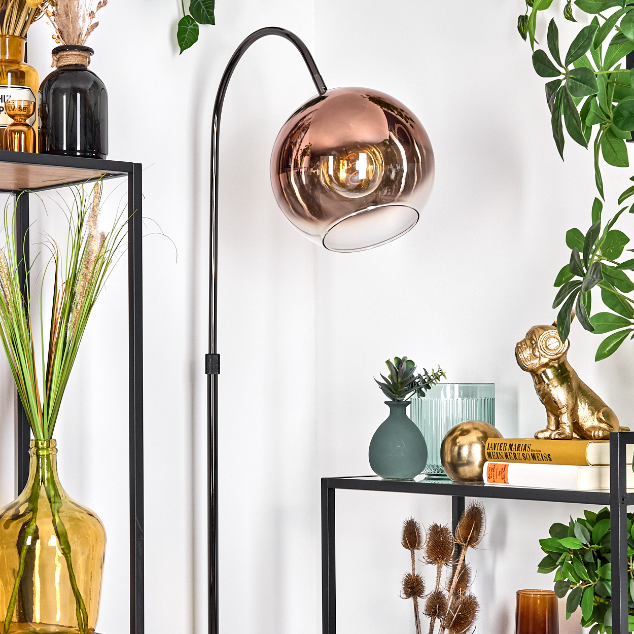 Ein modernes Zimmer mit Stehlampe, Kupferfarbenem Schirm, Regalen mit Pflanzen und Dekoration. Grüne Pflanzen an der Wand.