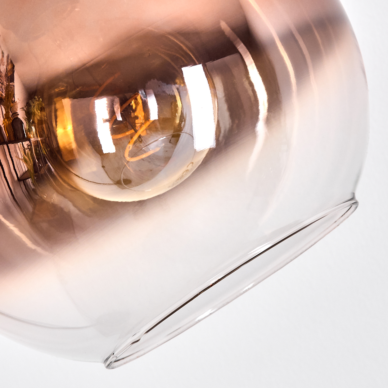 Nahaufnahme einer Glasleuchte mit einer Glühbirne. Das Glas ist klar mit einem Farbverlauf von Orange und Weiß. Der Hintergrund ist weiß.