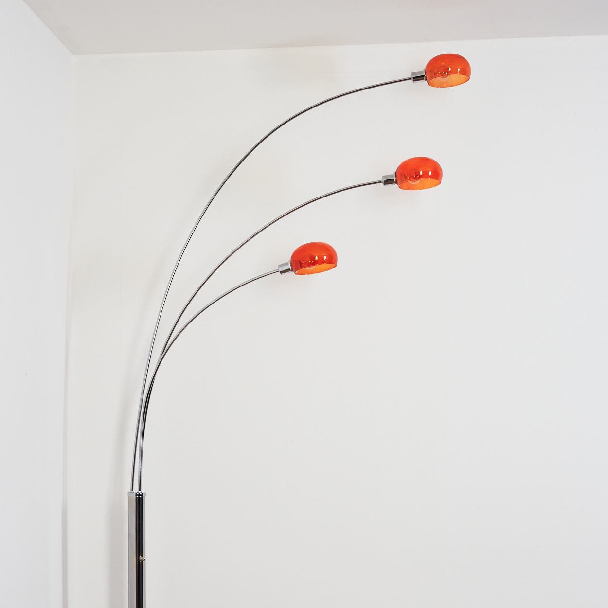 Eine moderne Stehlampe mit drei gebogenen Armen. Jeder Arm hält ein orangefarbenes, kuppelförmiges Licht. Die Basis ist schwarz und chrom.