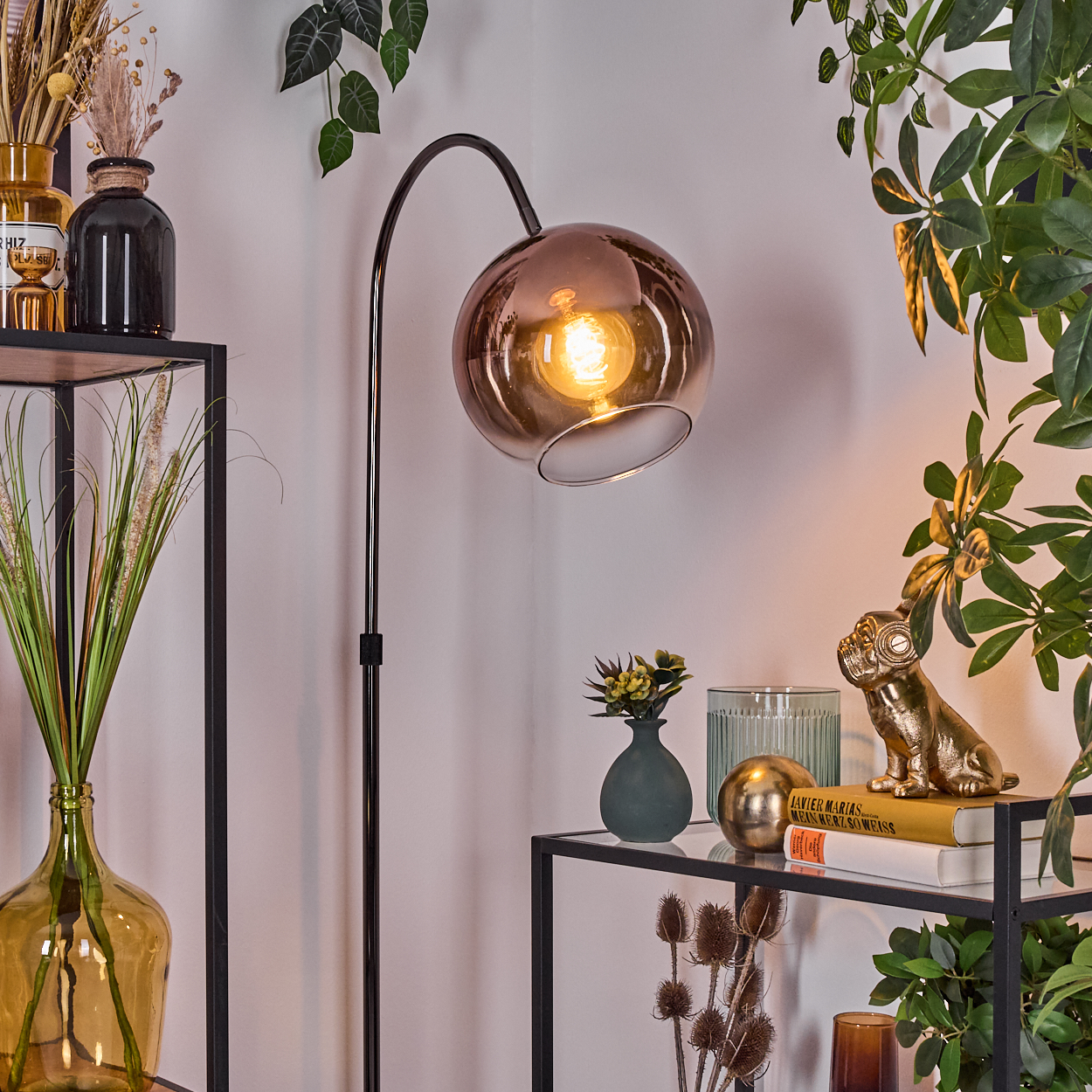 Eine moderne Innenecke mit Stehlampe, Pflanzen und Dekorationsartikeln auf Regalen. Eine goldene Hundestatue sitzt auf Büchern.
