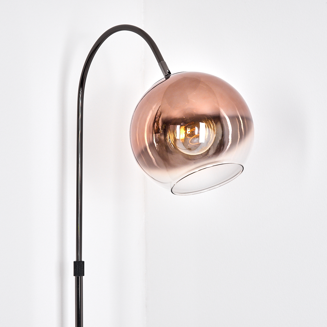 Eine moderne Stehlampe. Sie hat einen dunklen Metallrahmen und einen kupferfarbenen Glasschirm. Der Hintergrund ist weiß.