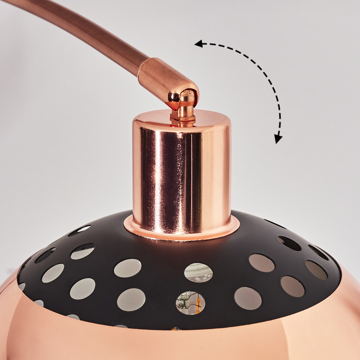 Nahaufnahme einer Lampe. Sie hat eine Kupferoberfläche, einen schwarzen Schirm mit Löchern und einen verstellbaren Arm. Der Hintergrund ist weiß.