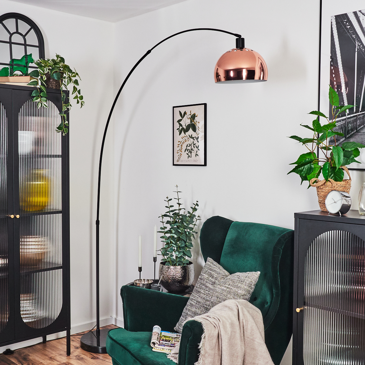Ein Wohnzimmer mit grünem Sessel, Kupferlampe und schwarzen Schränken. Pflanzen und Bilder schmücken den Raum.