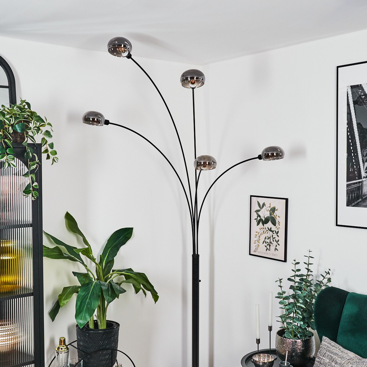 Ein modernes Wohnzimmer mit schwarzer Stehlampe, Pflanzen und gerahmten Kunstwerken. Die Lampe hat fünf Kugelleuchten. Grüne Pflanzen.