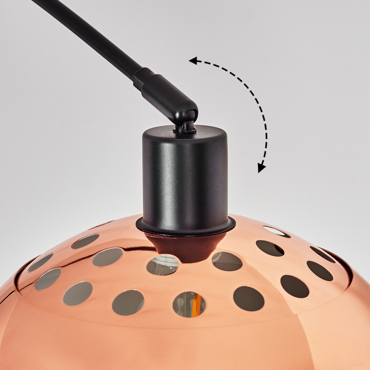 Nahaufnahme einer Kupferlampe mit schwarzem Arm und gestricheltem Pfeil, der ihre Bewegung anzeigt. Sie hat runde Löcher.