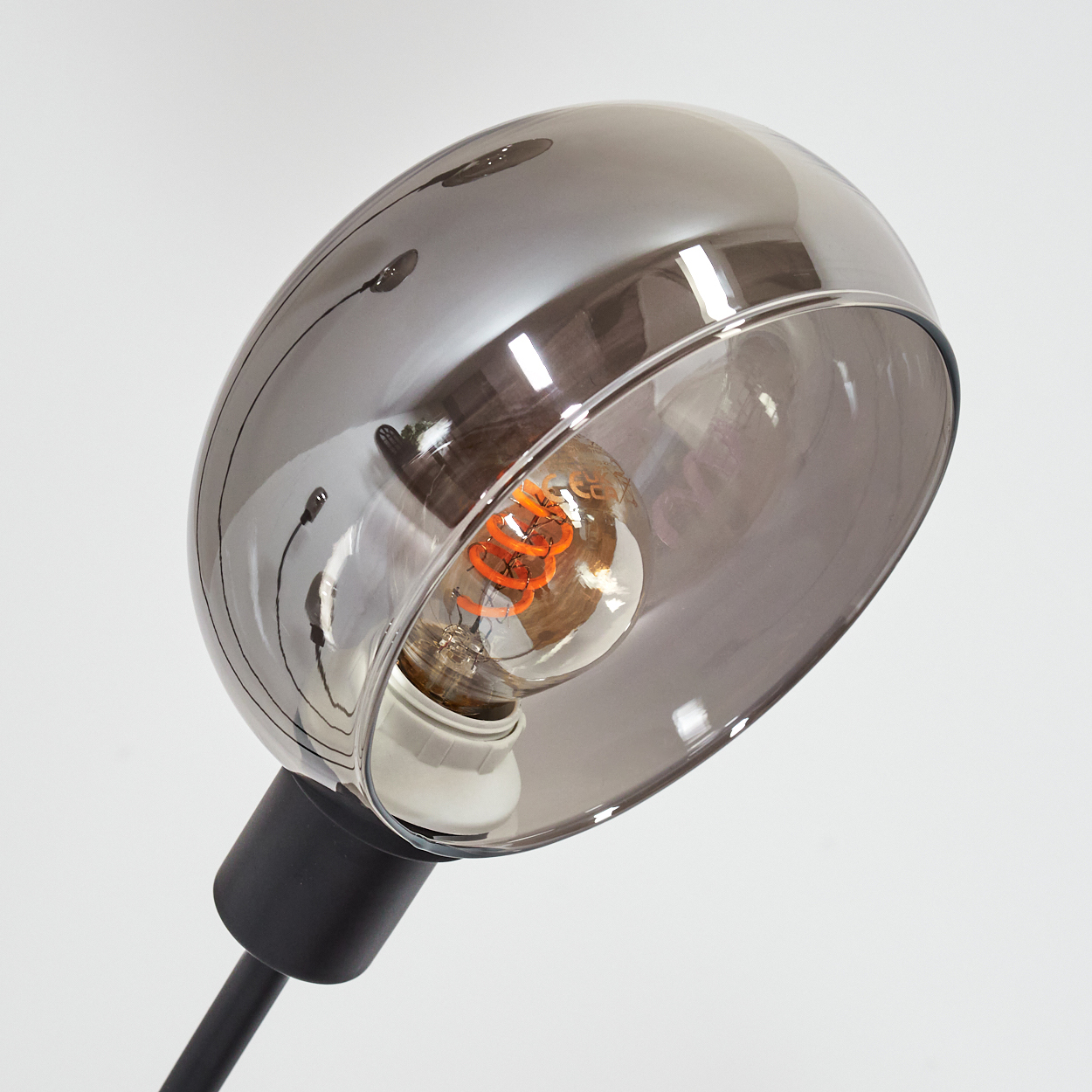 Eine moderne Lampe mit grauem Schirm und einer sichtbaren orangefarbenen Glühbirne vor weißem Hintergrund.