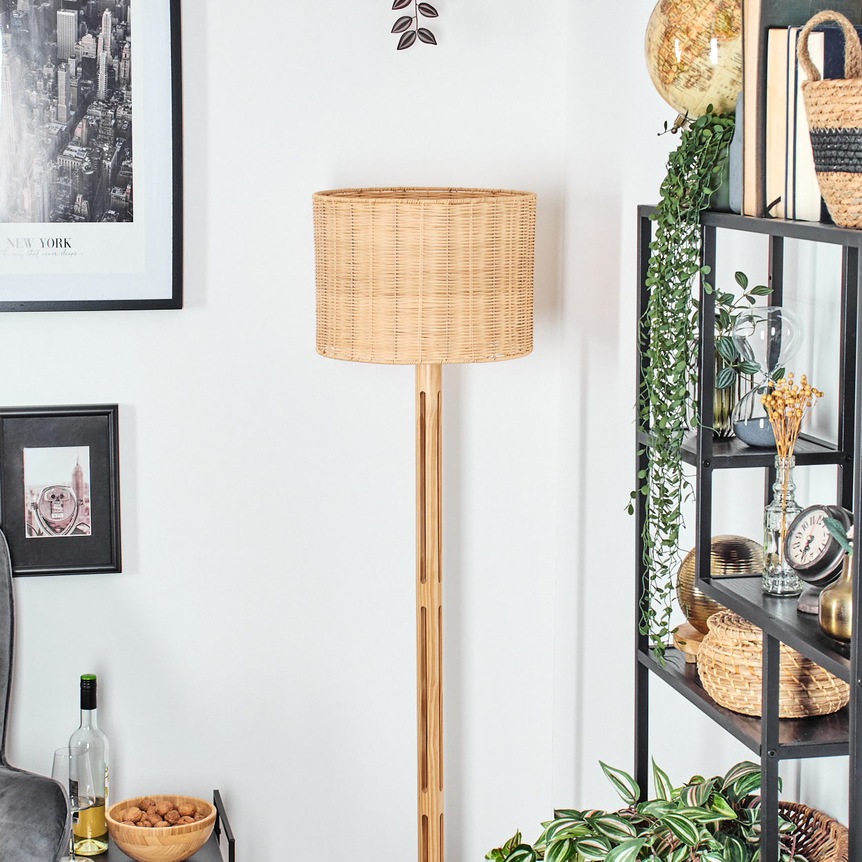 Ein Raum mit einer Lampe, einem Regal mit Dekorationen und gerahmten Bildern an der Wand. Die Lampe hat einen gewebten Schirm.