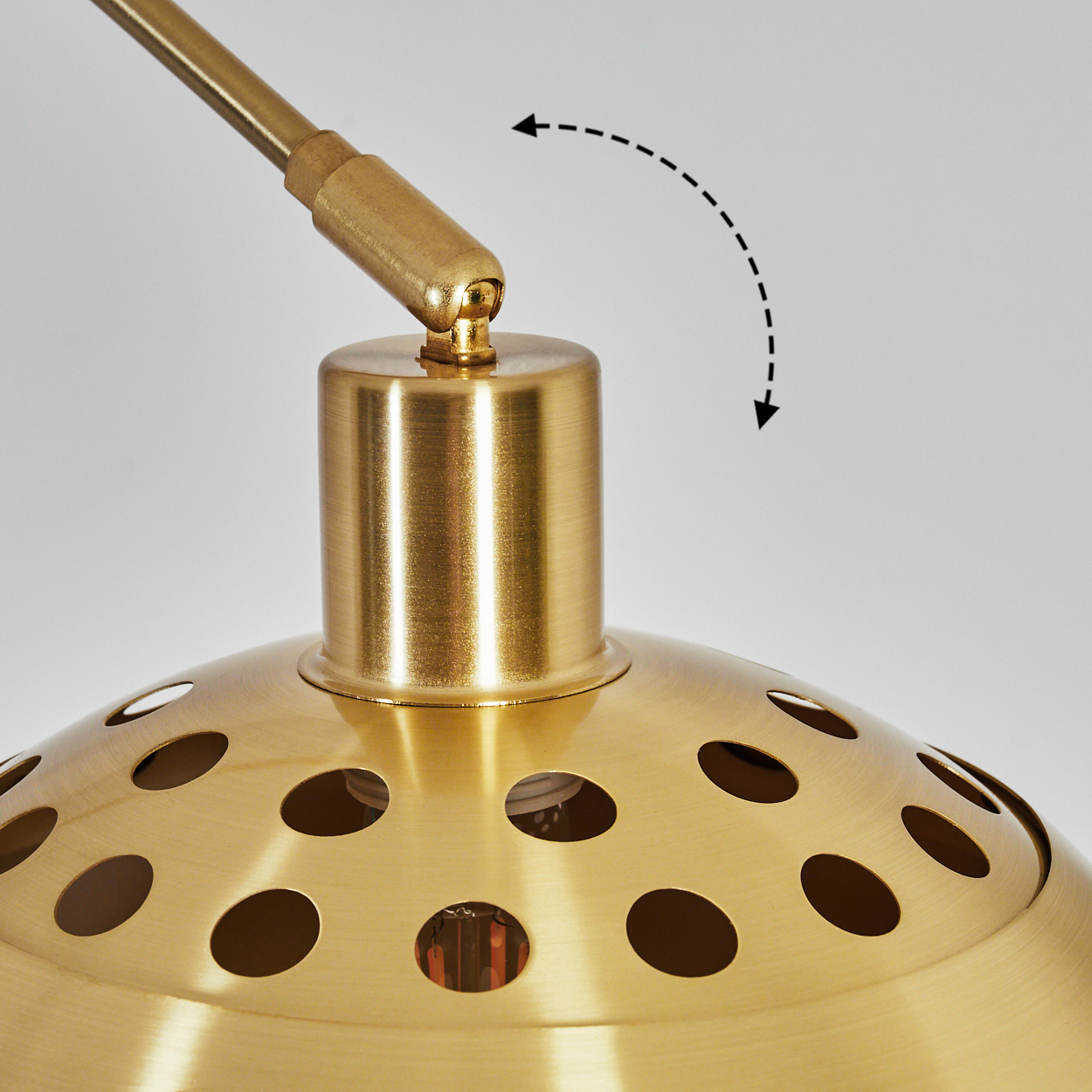 Nahaufnahme einer goldenen Lampe mit perforiertem Lampenschirm. Es hat einen gebogenen Arm und ein Drehgelenk. Der Hintergrund ist weiß.