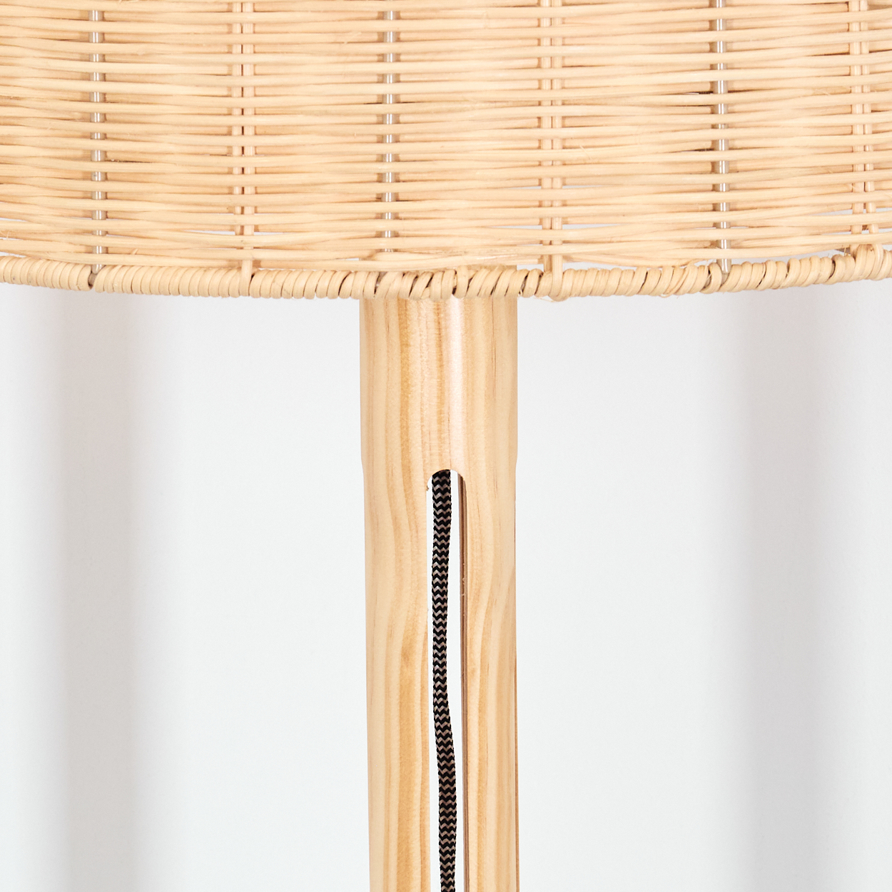 Nahaufnahme einer Lampe. Lampenschirm aus Korbgeflecht auf einem Holzpfahl. Ein schwarzes Kabel verläuft den Pfahl hinunter. Weißer Hintergrund.
