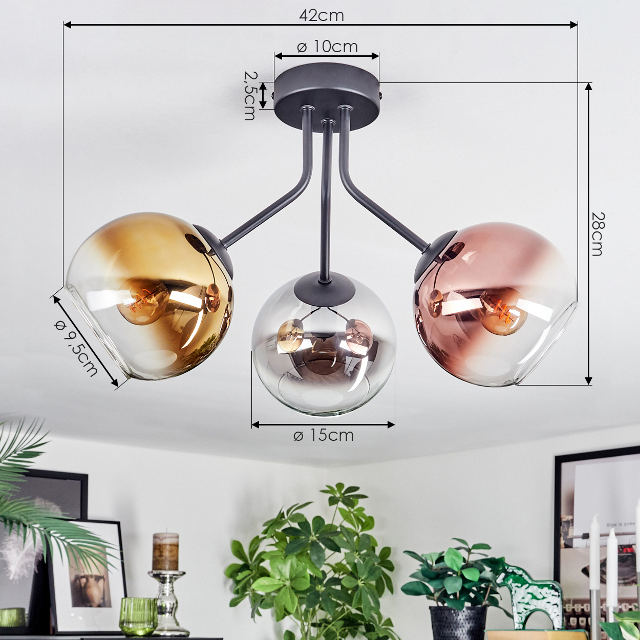 Eine moderne Deckenlampe mit drei Glaskugeln. Die Schirme sind bernsteinfarben, silber und roségold. Die Lampe ist an einer weißen Decke montiert.