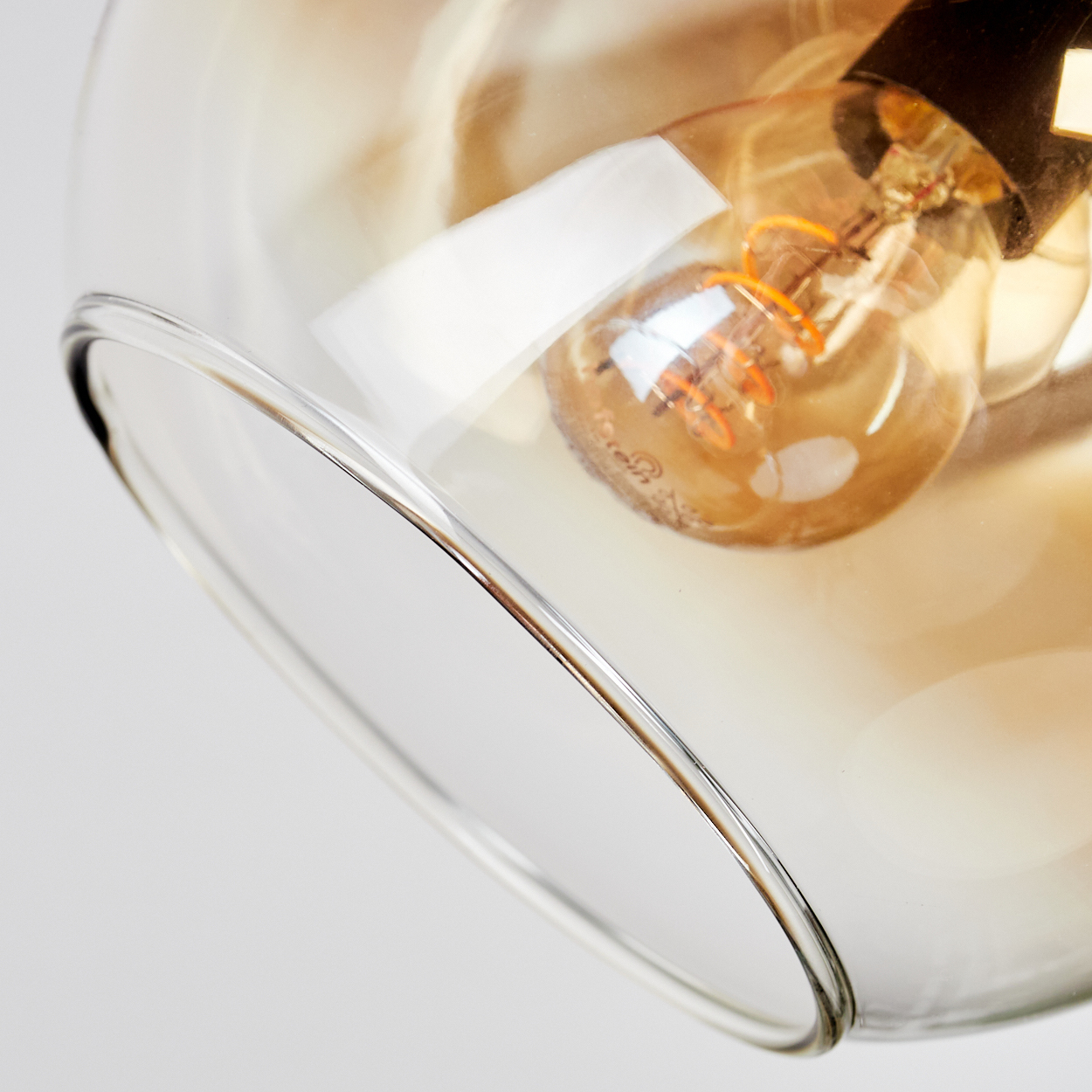 Nahaufnahme eines Glasschirms mit einer Glühbirne. Das Glas ist klar mit einem Braunstich, die Glühbirne leuchtet.