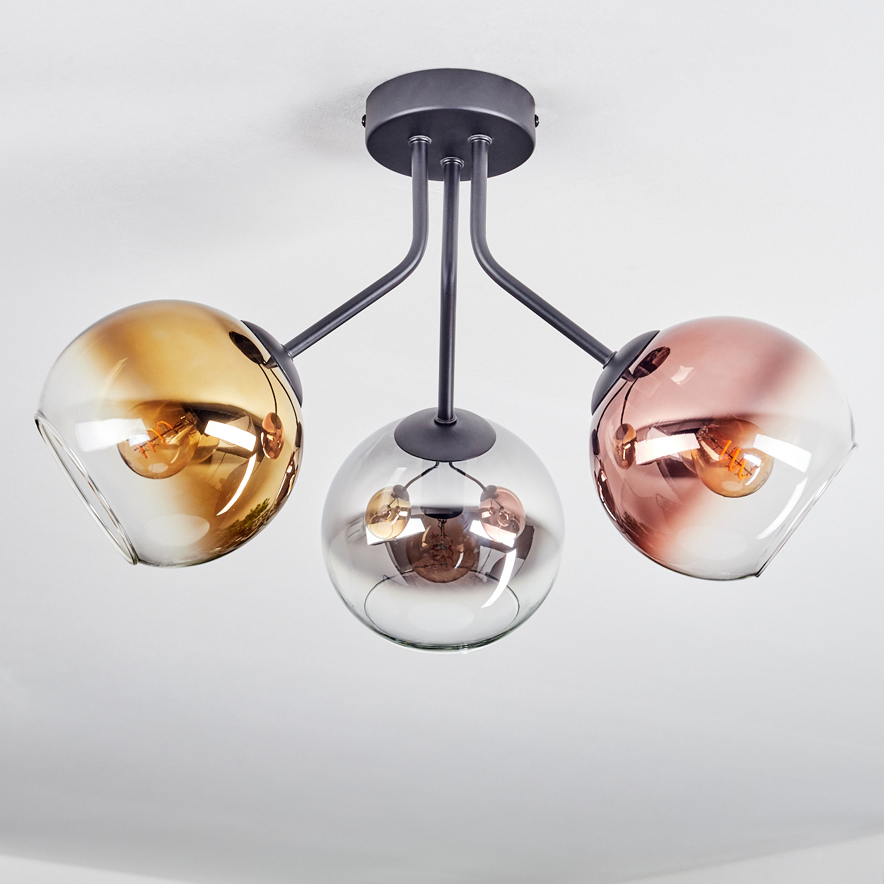 Moderne Deckenleuchte mit drei Glasschirmen in Gold, Silber und Roségold. Jede Schirm hat eine sichtbare Glühbirne.