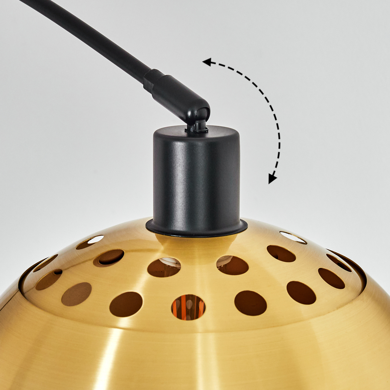 Nahaufnahme einer Lampe. Sie hat einen goldenen Schirm mit Löchern, einen schwarzen Arm und einen schwarzen zylindrischen Sockel. Pfeile zeigen die Bewegung an.