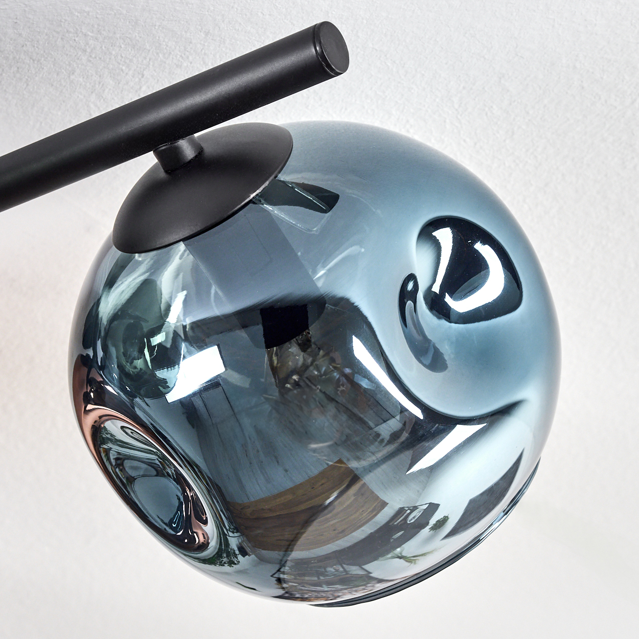 Eine moderne Lampe mit blauem Glaskugel und schwarzem Metallarm. Die Lampe steht vor einer weißen Wand.
