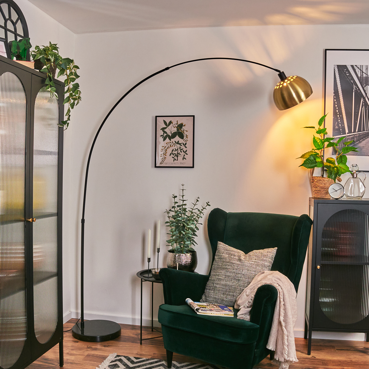 Ein grüner Sessel mit Decke und Kissen, eine schwarze Lampe, ein Schrank und Pflanzen in einem Raum.