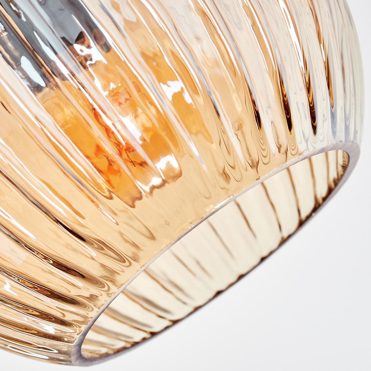 Nahaufnahme eines Lampenschirms aus Glas mit vertikalen Rippen. Das Glas ist bernsteinfarben und reflektiert Licht. Der Hintergrund ist weiß.
