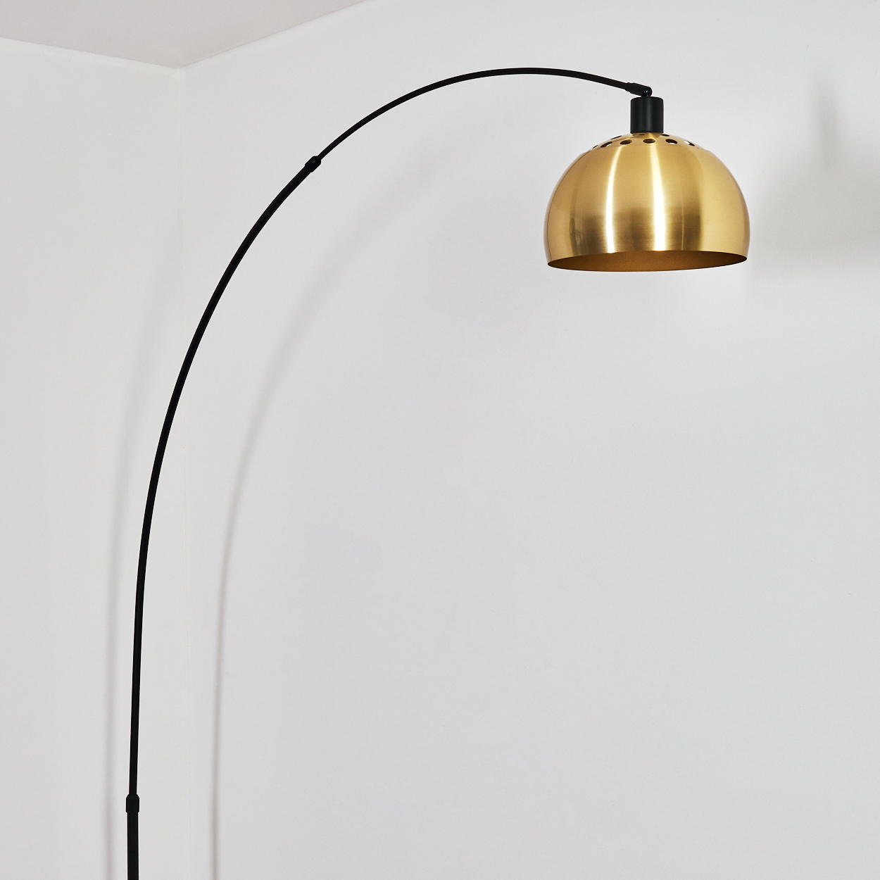 Eine moderne Bogenlampe mit goldenem Lampenschirm. Die Lampe ist schwarz, die Wand ist weiß. Der Lampenschirm ist golden und kuppelförmig.