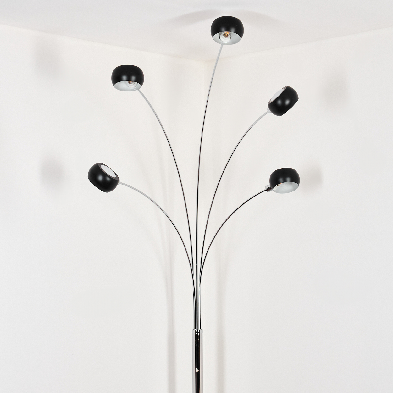 Eine moderne Stehlampe mit fünf schwarzen, kugelförmigen Lampenschirmen und Chromstielen. Sie steht in der Ecke eines weißen Raumes.