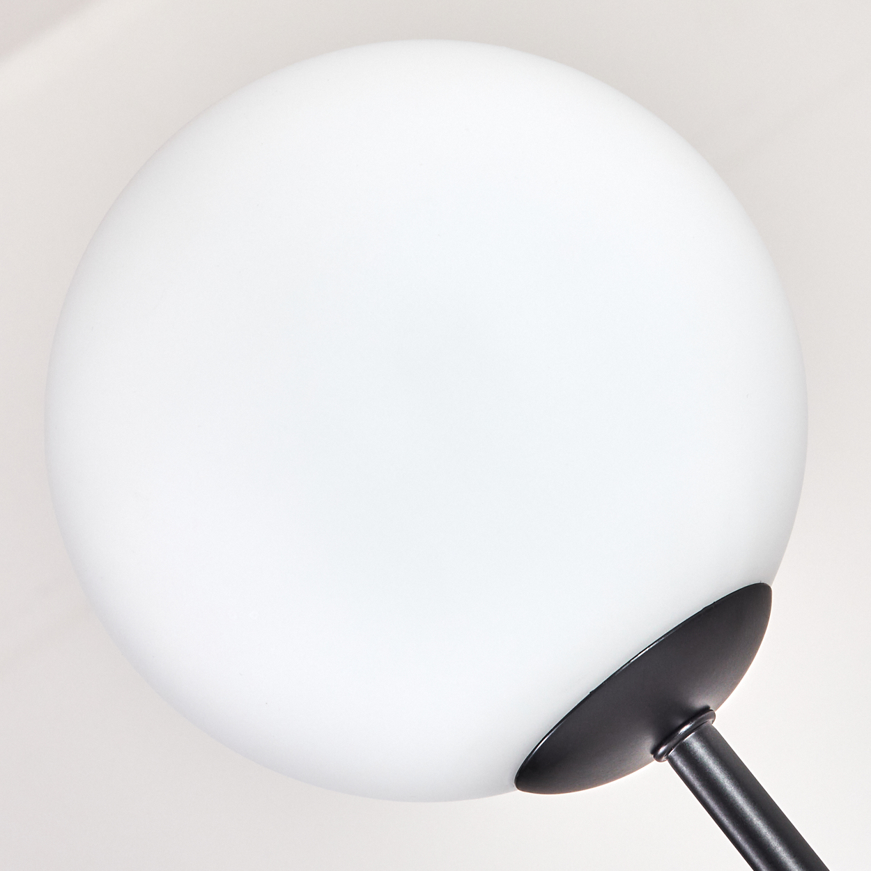 Nahaufnahme einer weißen Kugel-Lampe mit schwarzem Sockel und Stiel. Der Hintergrund ist ein sanftes Weiß.