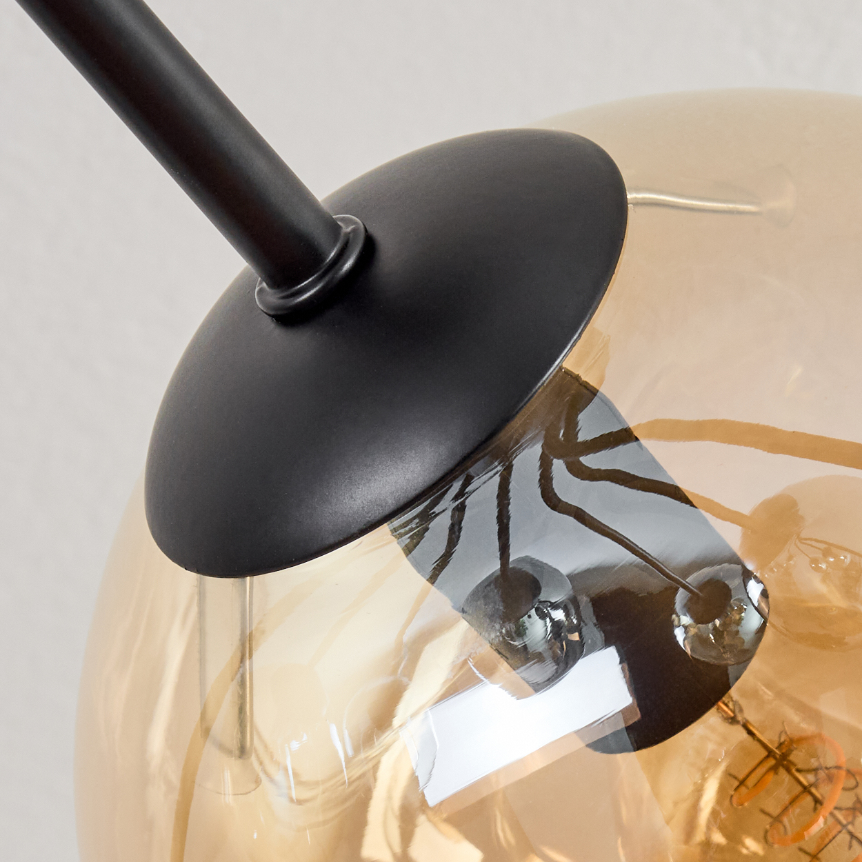 Nahaufnahme einer modernen Lampe. Sie hat einen schwarzen Arm und einen runden, bernsteinfarbenen Glasschirm. Der Hintergrund ist ein neutrales Grau.