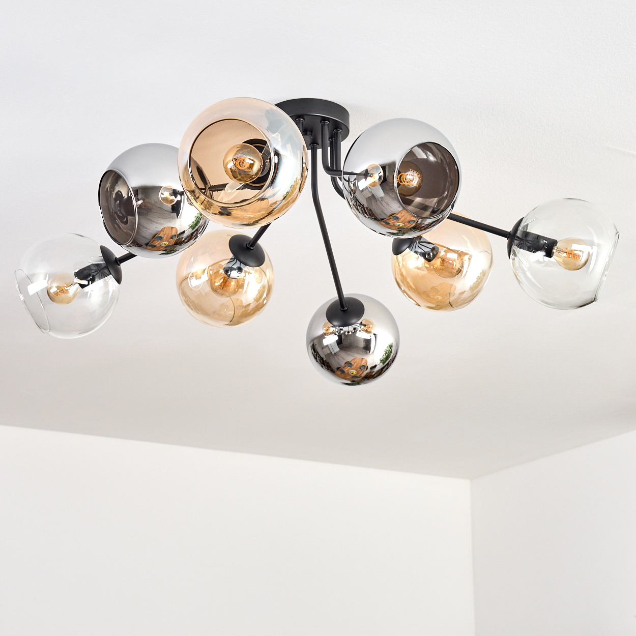 Moderne Deckenleuchte mit mehreren Glaskugelschirmen in Silber, Gold und Klar, beleuchtet mit warmem Licht, vor weißer Decke.