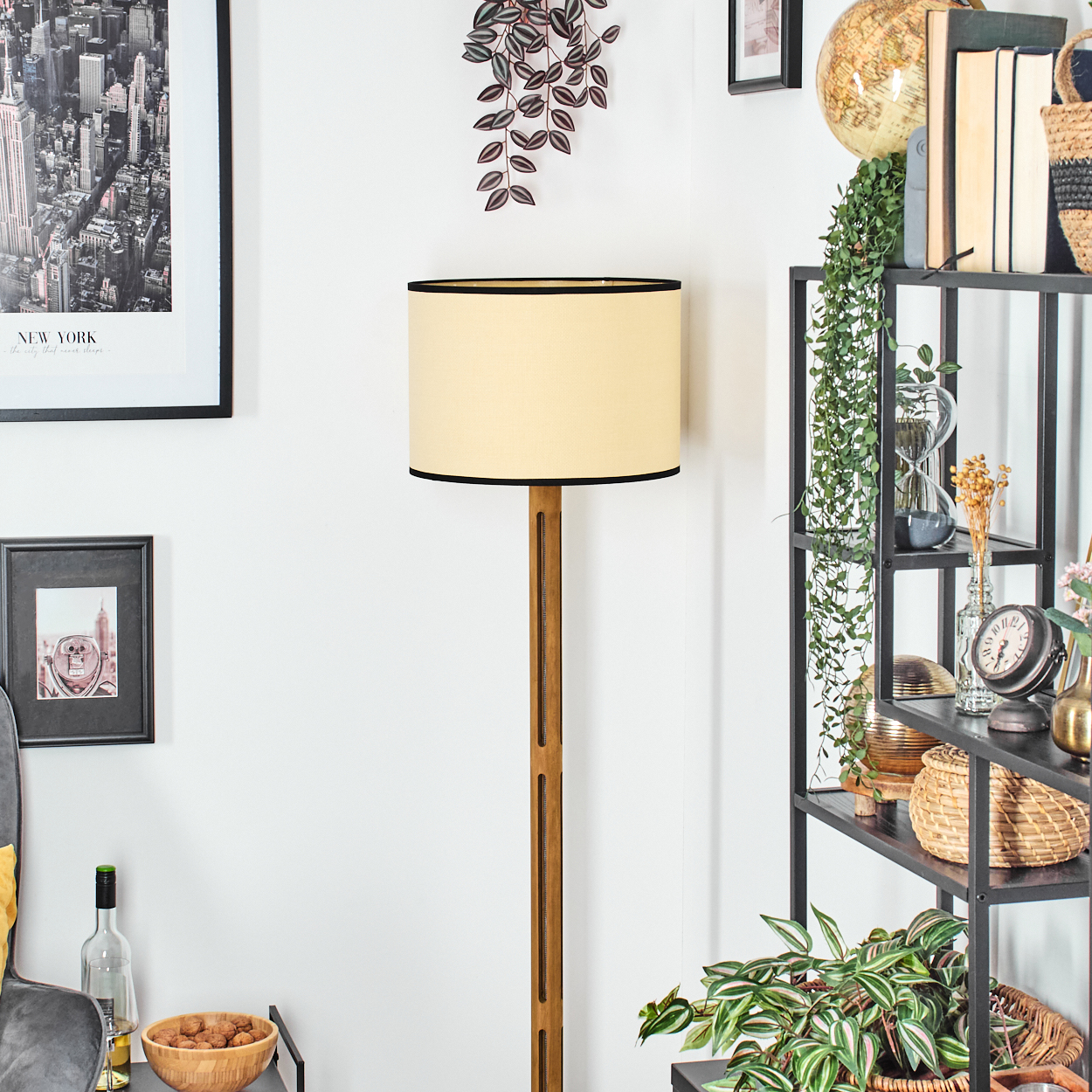 Ein Raum mit Stehlampe, Regalen mit Gegenständen und gerahmten Bildern. Ein New York-Poster hängt an der Wand.