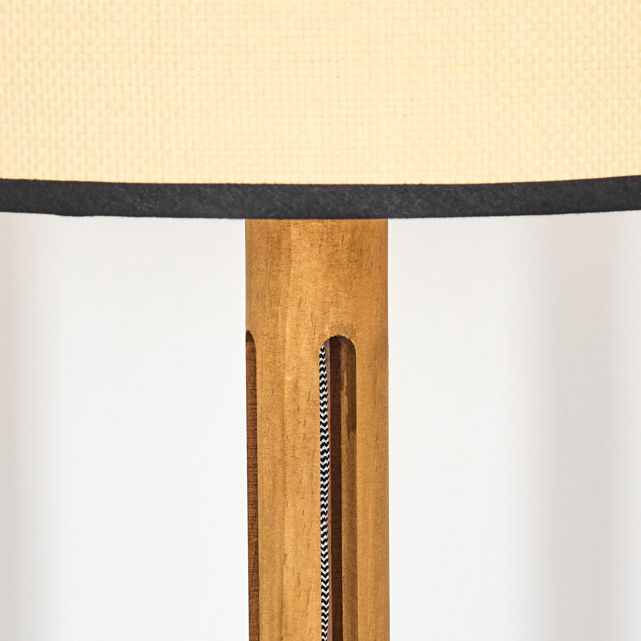 Nahaufnahme einer Lampe. Beiger Lampenschirm mit schwarzem Rand sitzt auf einem Holzpfosten mit gemustertem Kabel.