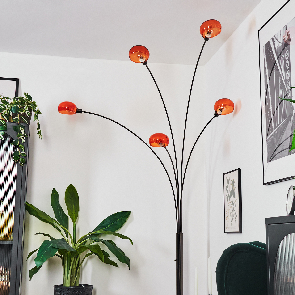 Ein modernes Wohnzimmer mit einer schwarzen Stehlampe mit orangefarbenen Kugeln. Eine Topfpflanze, ein gerahmtes Bild und ein Stuhl sind sichtbar.