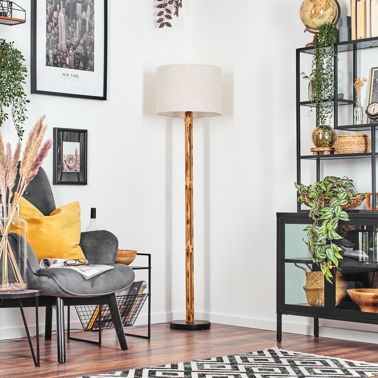 Raumecke mit Lampe, Stuhl und Regal. Ein New York-Bild hängt an der Wand. Pflanzen und ein Teppich sind vorhanden.