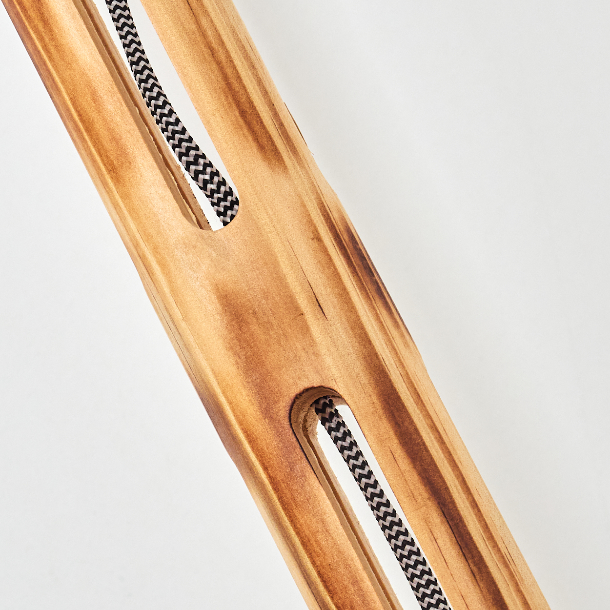 Nahaufnahme eines Holzbalkens mit zwei rechteckigen Aussparungen. Ein schwarz-weißes Kabel verläuft durch die Aussparungen vor weißem Hintergrund.