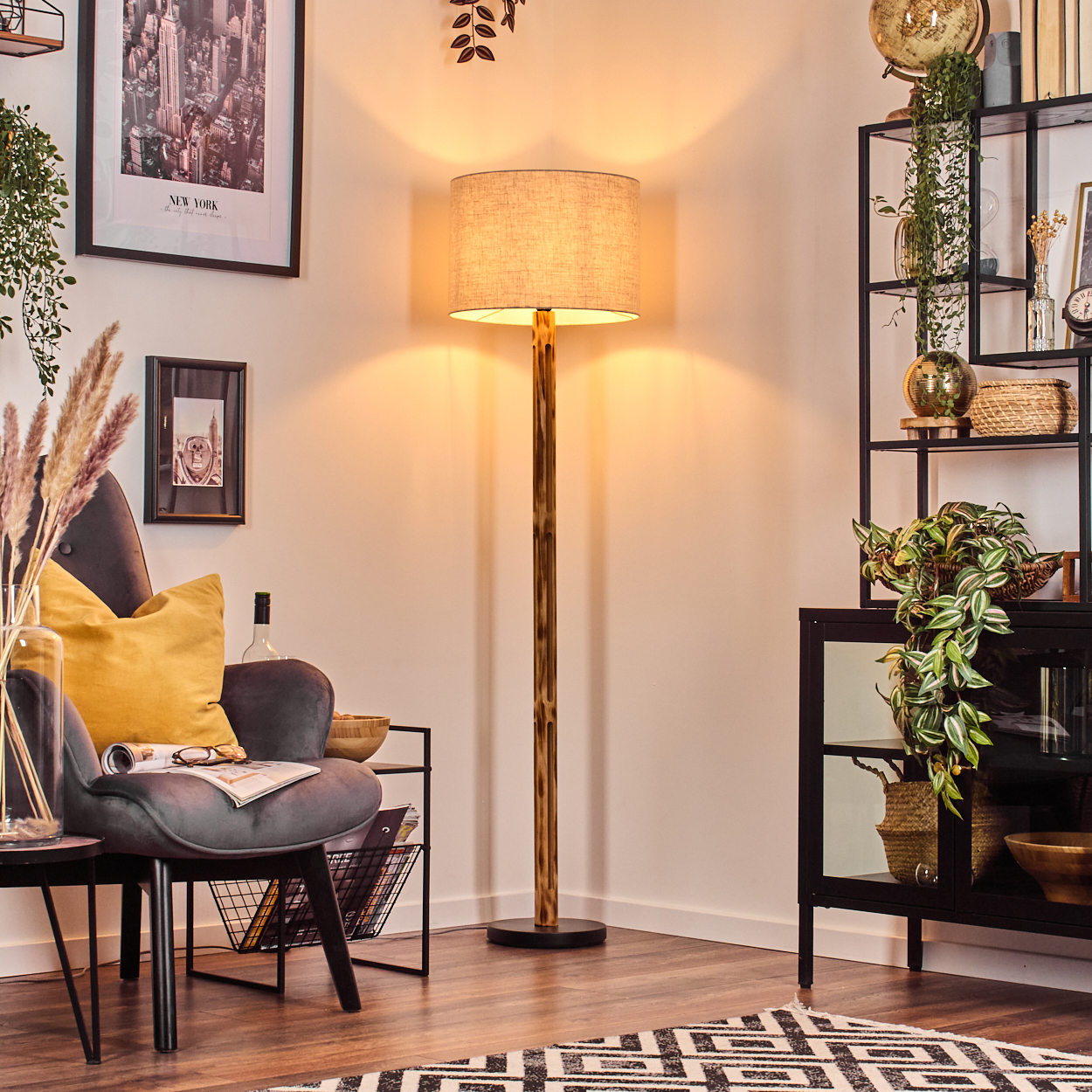 Ein Wohnzimmer mit einer Stehlampe. Es gibt einen grauen Sessel mit einem gelben Kissen und ein schwarzes Bücherregal.
