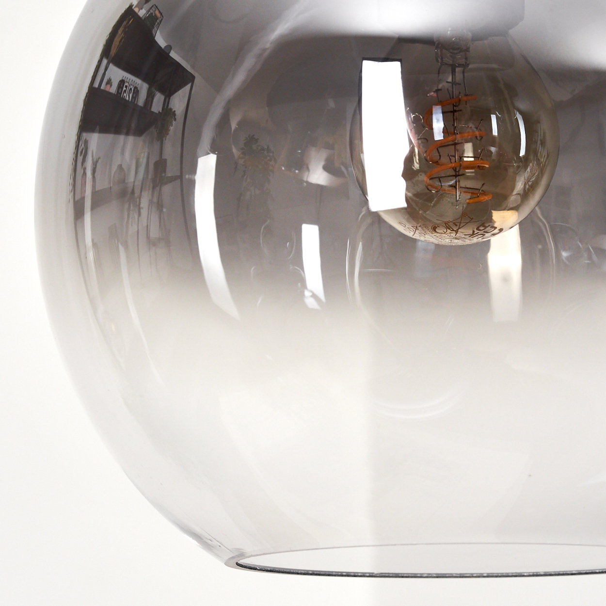 Nahaufnahme einer Glas-Hängelampe. Die Lampe hat eine Glühbirne im Inneren. Das Glas ist klar und rauchig.