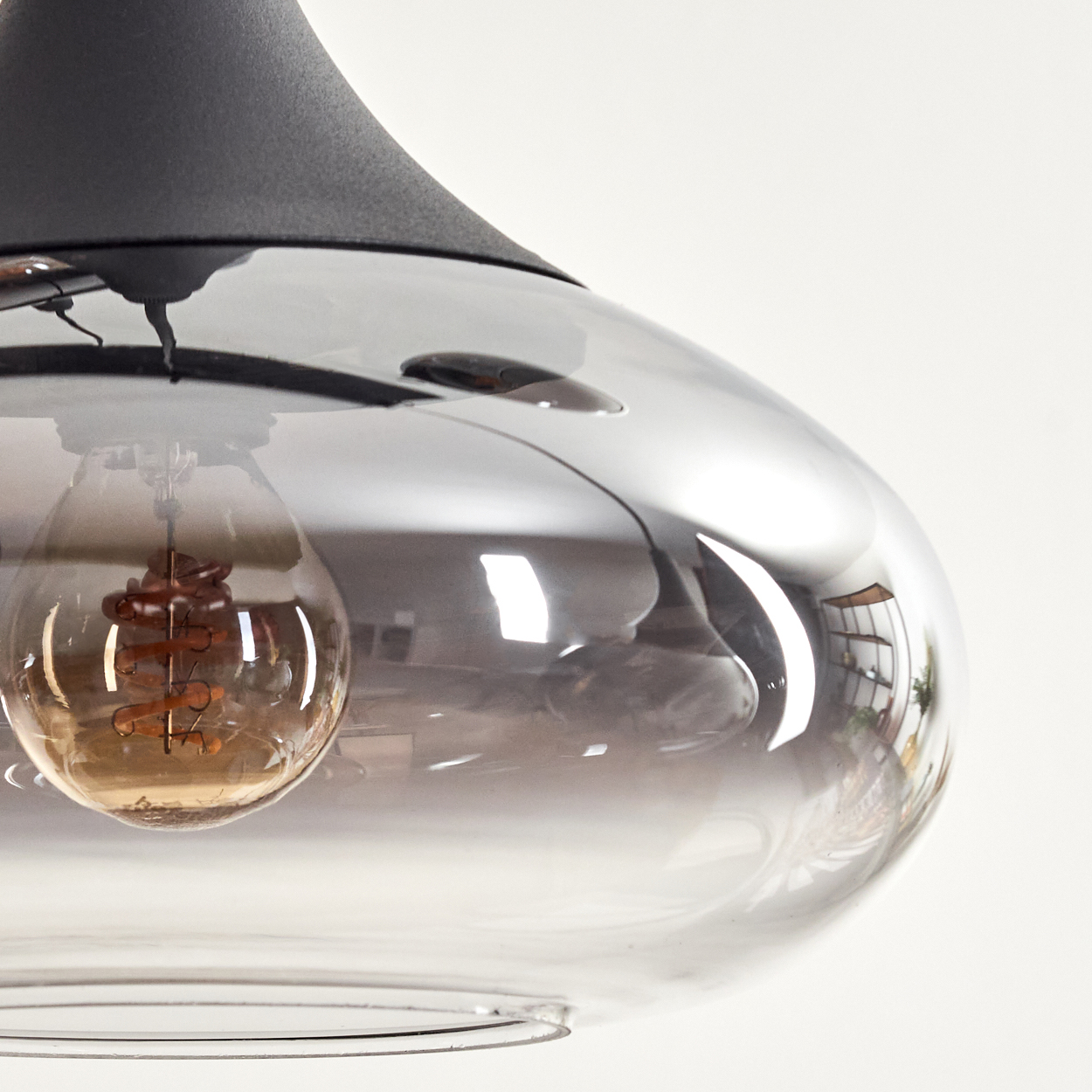 Eine moderne Pendelleuchte mit rauchfarbenem Glasschirm und sichtbarer Edison-Glühbirne. Das Gerät hat einen schwarzen Deckel vor weißem Hintergrund.