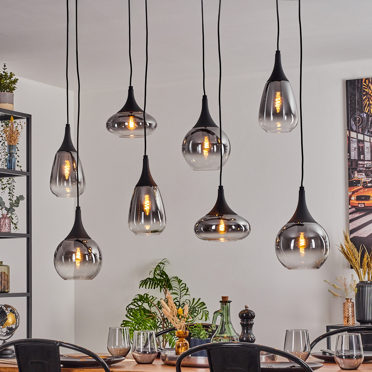 Esszimmer mit mehreren Hängelampen. Tisch mit Gläsern und Pflanzen. Wandkunst und Regale im Hintergrund.